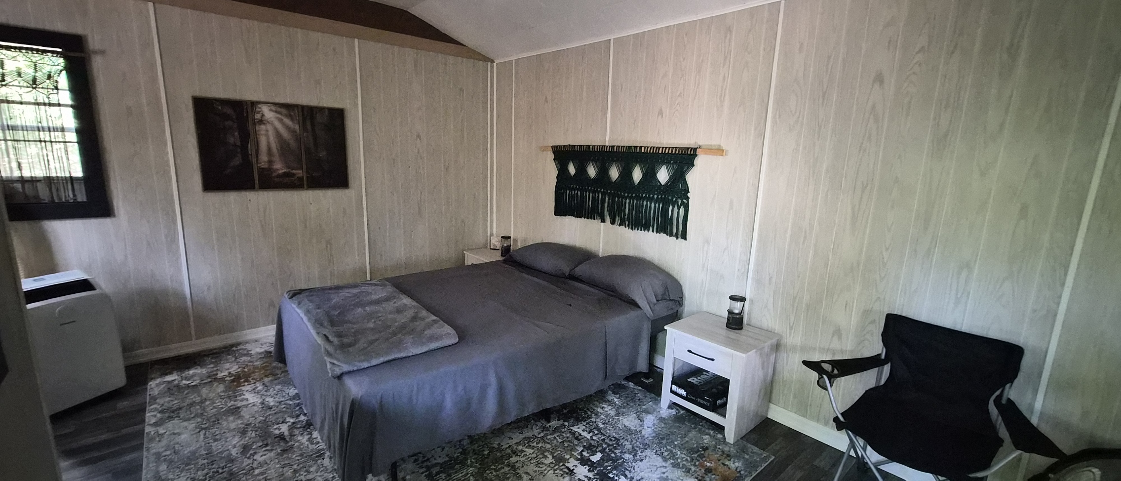 Queen bed with a macramé headboard and trimmed window inside the cabin