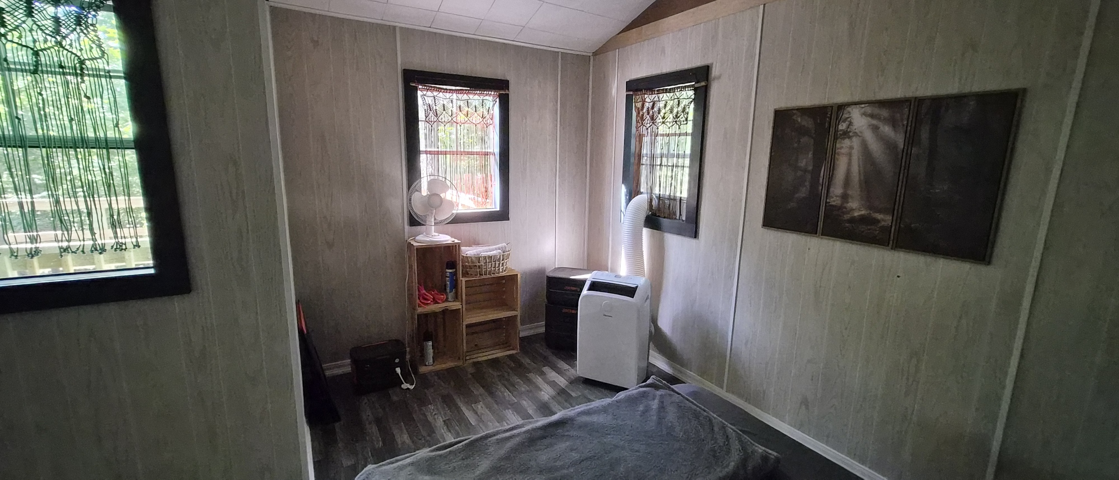 Finished cabin interior with trimmed windows, macramé curtains, fan, and portable air conditioner